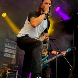 Sänger performt stehend auf einer Monitorbox im violetten Licht bei Rock im Onnergrond