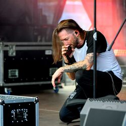 Tätowierter Musiker kniet auf der Bühne zwischen Flightcases bei Rock im Onnergrond