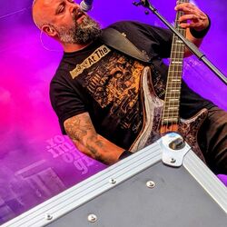 Bassist singt und spielt Bass stehend auf einem Boxenturm im violetten Licht bei Rock im Onnergrond